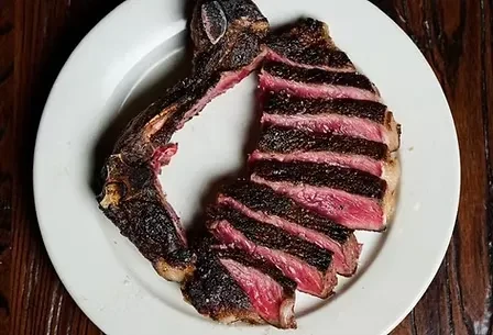 A sliced, medium-rare steak on a white plate with a bone.