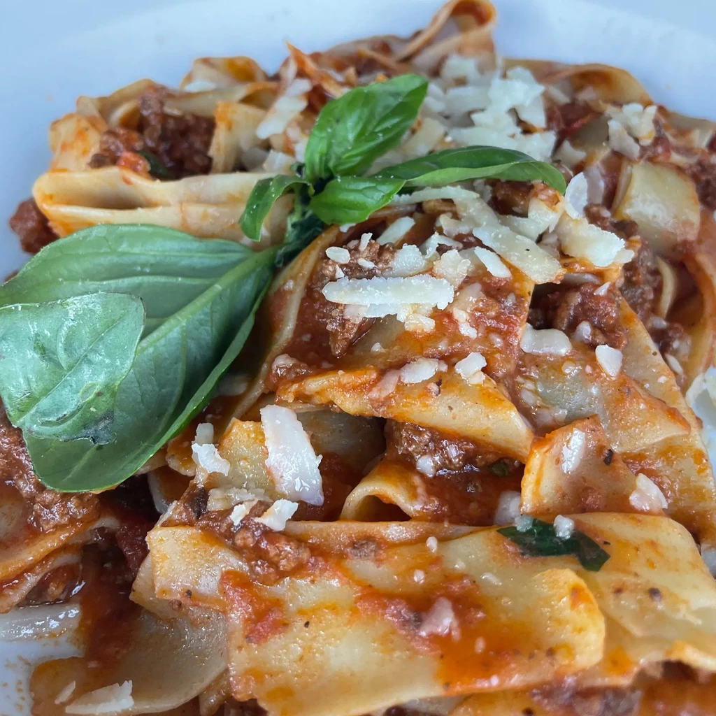Close-up of pappardelle pasta with Bolognese sauce, Parmesan cheese, and basil.