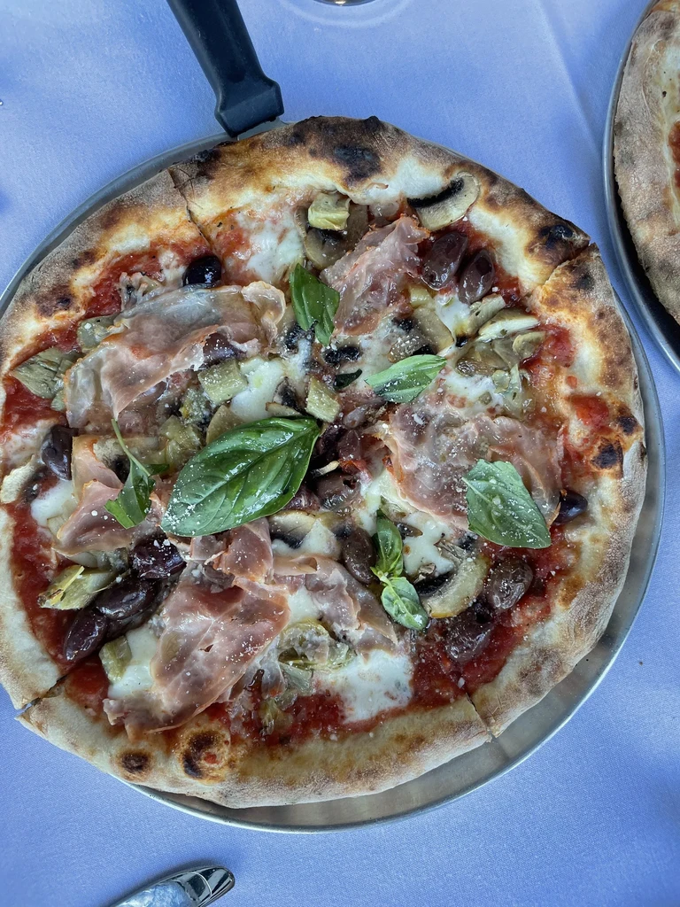Close-up of a pizza with prosciutto, mushrooms, olives, and basil.