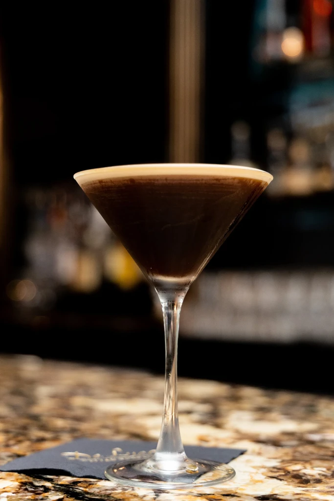 An espresso martini with a foamy top, on a marble bar.