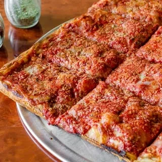 A freshly baked square Sicilian pizza, sliced, on a metal tray.