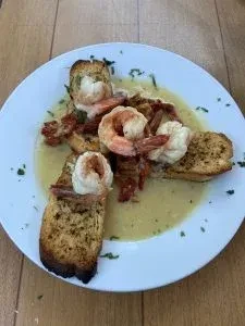Shrimp scampi in a light sauce with toasted bread on a white plate.