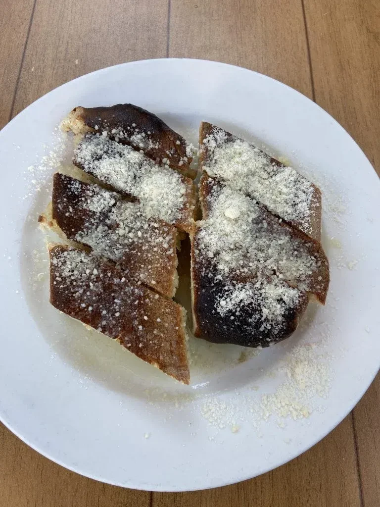 Burnt garlic bread with parmesan cheese on a white plate.