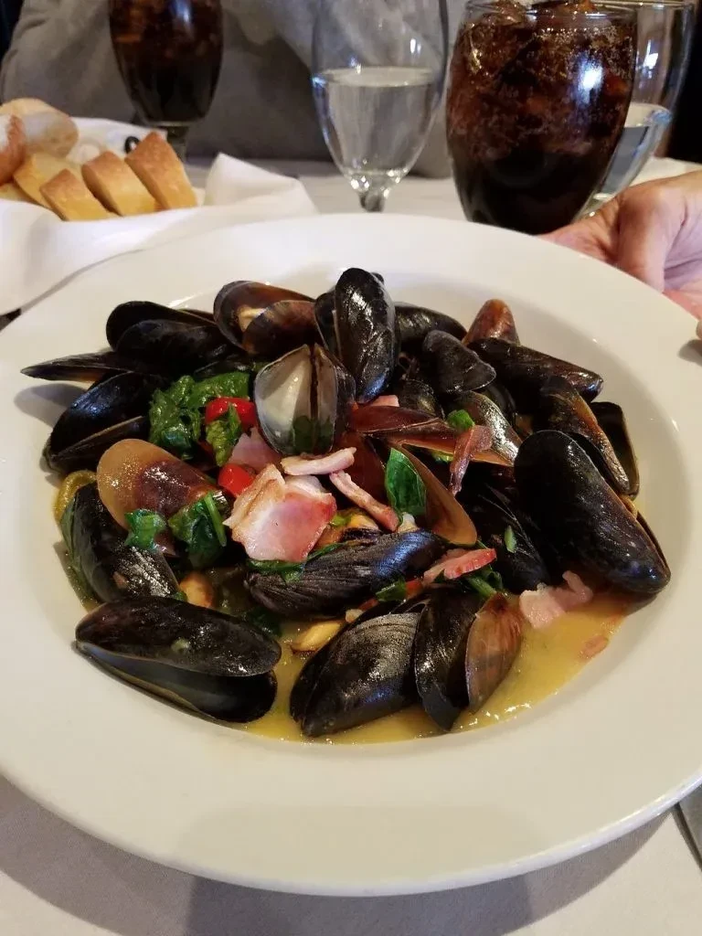 A plate of mussels with bacon and greens in a light sauce.