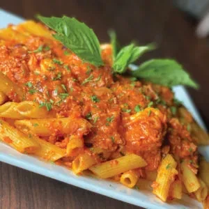 Penne pasta with a red sauce, basil leaves, and parsley garnish.