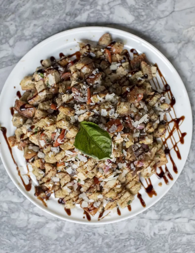 A plate of bread salad with tomatoes, cheese, basil, and balsamic glaze.