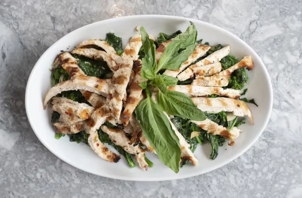 Grilled chicken breast strips with basil on a bed of greens.