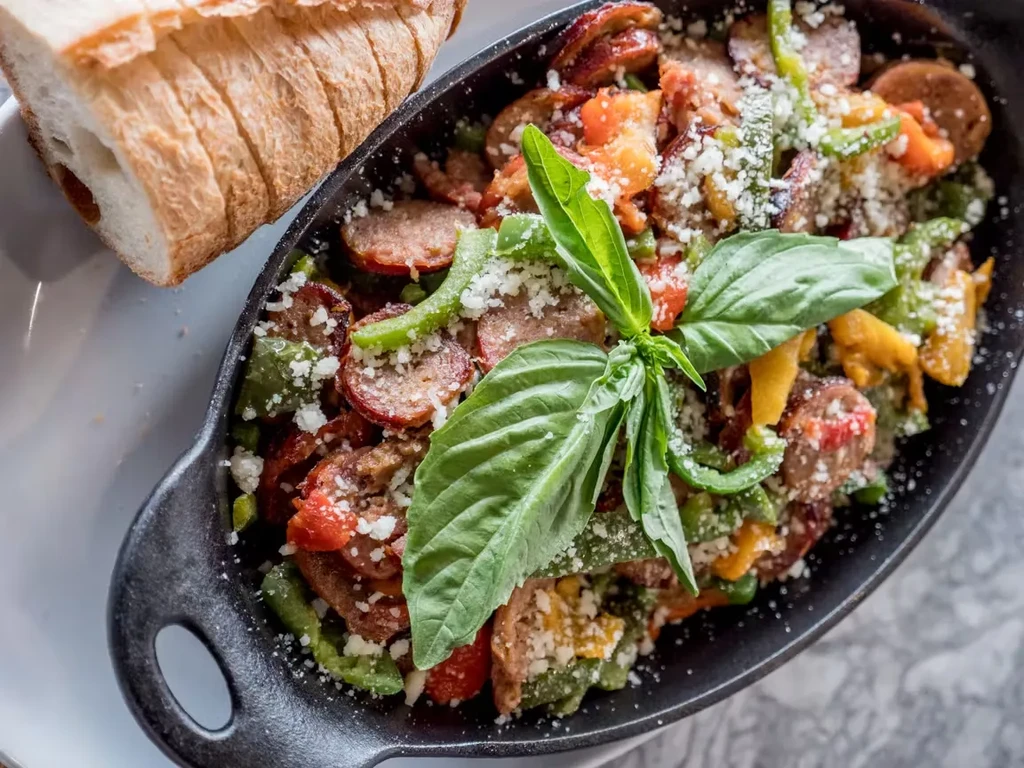 Sausage, peppers, and onions in a skillet with a side of bread.