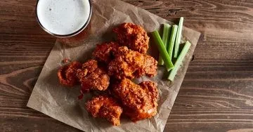 Overhead view of buffalo wings, celery, and a beer on a wooden table.