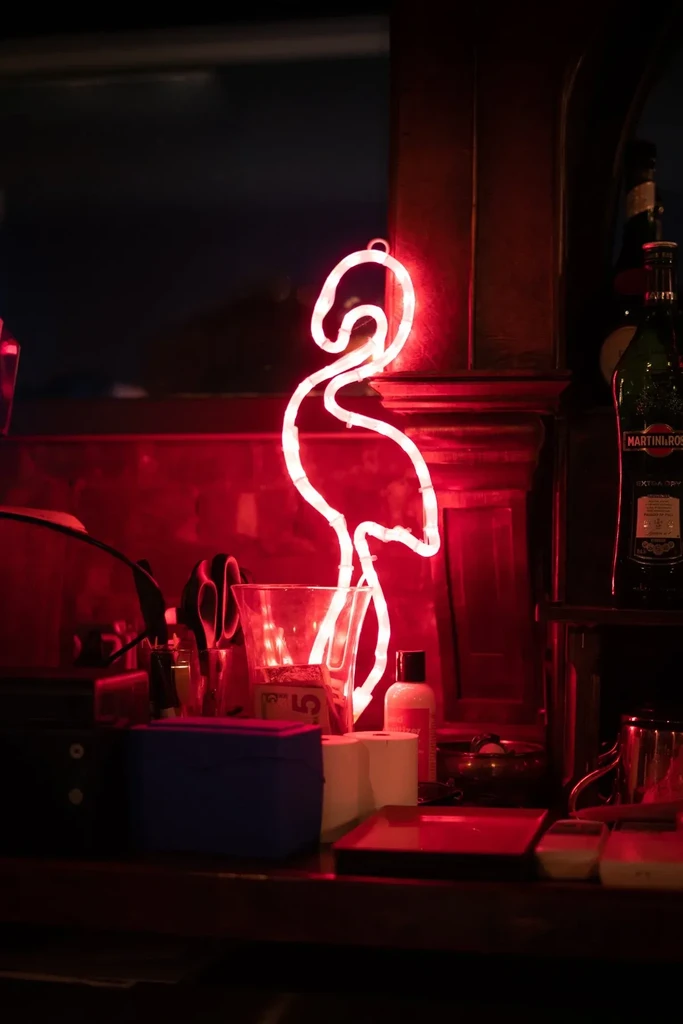A neon flamingo sign glows bright white in a dimly lit bar.