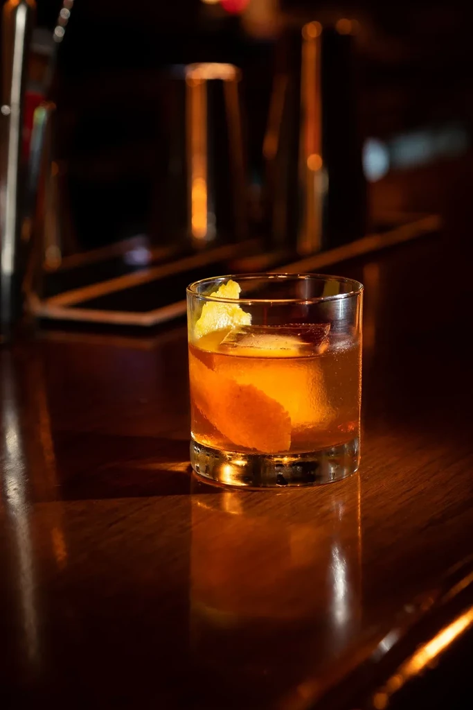 A cocktail in a glass with ice and an orange peel.