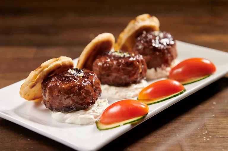 Three meatballs with flatbread, yogurt, and sliced tomatoes on a plate.