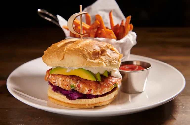 A salmon burger with avocado, fries, and ketchup on a white plate.