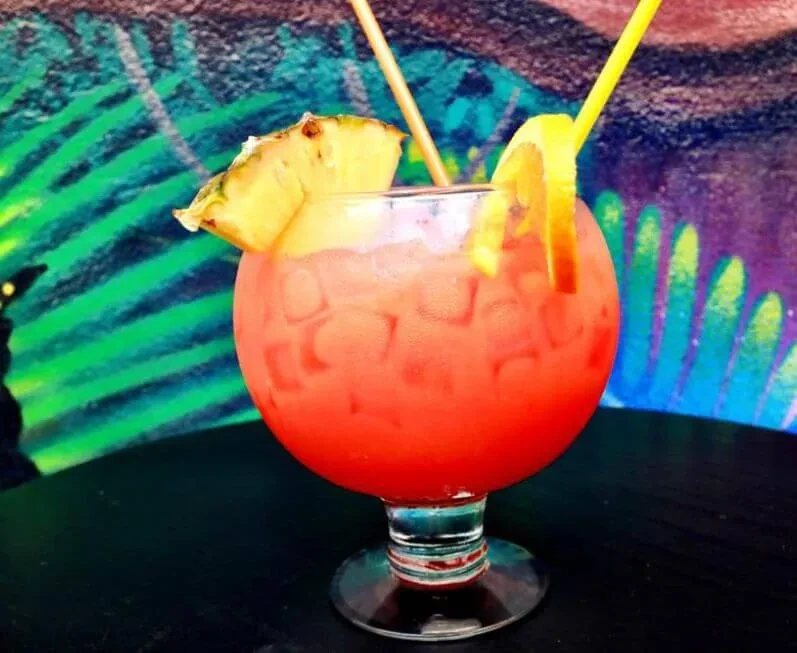 A red drink with pineapple and orange slices against a colorful background.