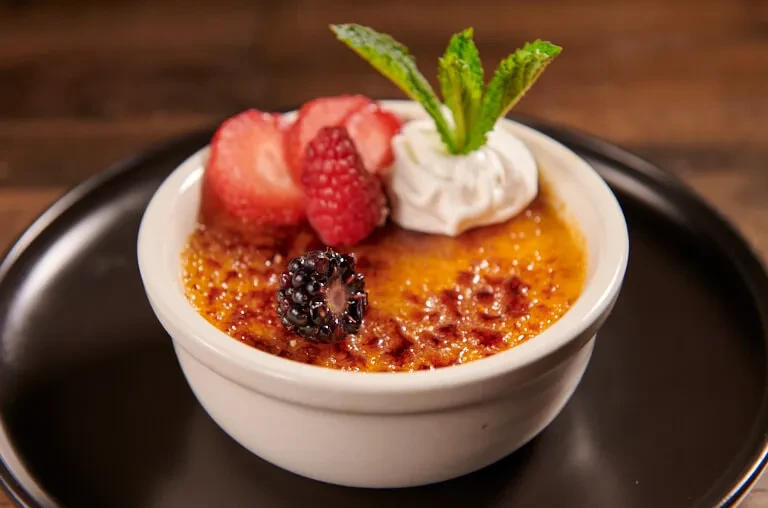 Creme brûlée in a ramekin with berries, whipped cream, and mint.
