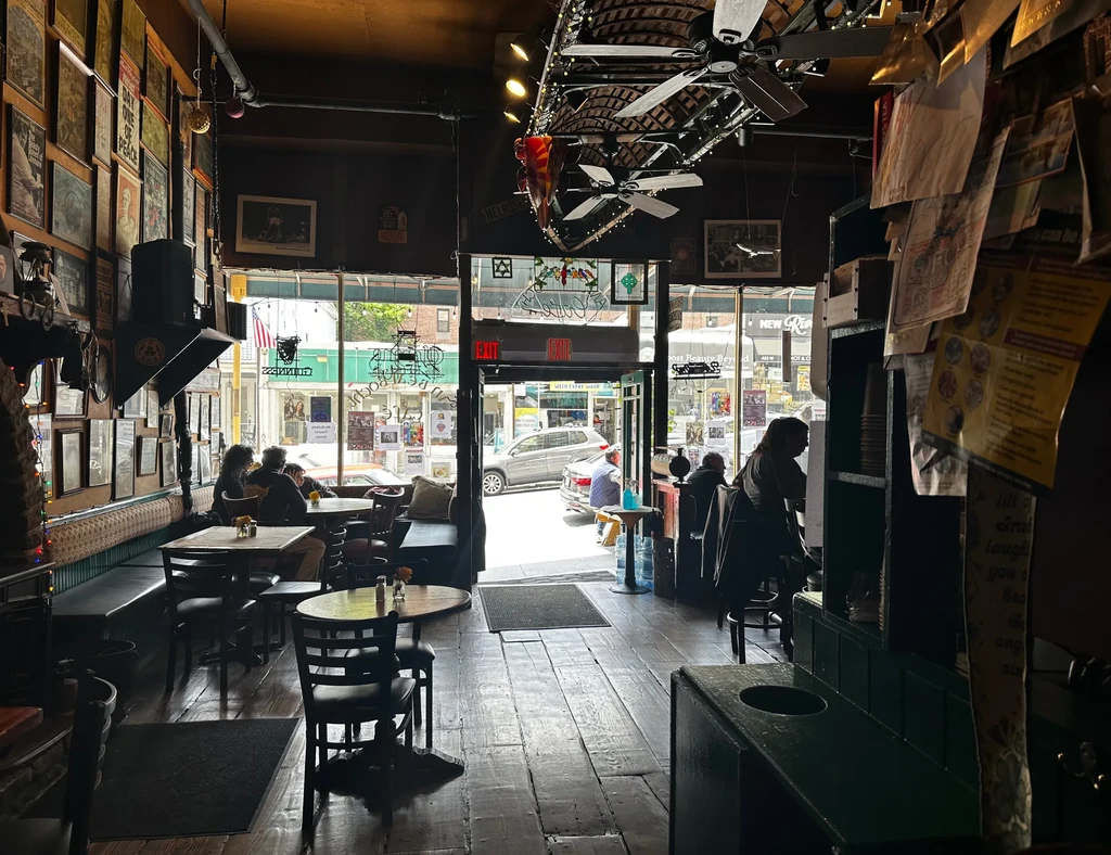 Patrons and workers inside a dark bar with large windows facing a street.