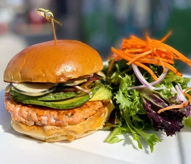 A salmon burger with avocado, zucchini, and a side salad on a white plate.
