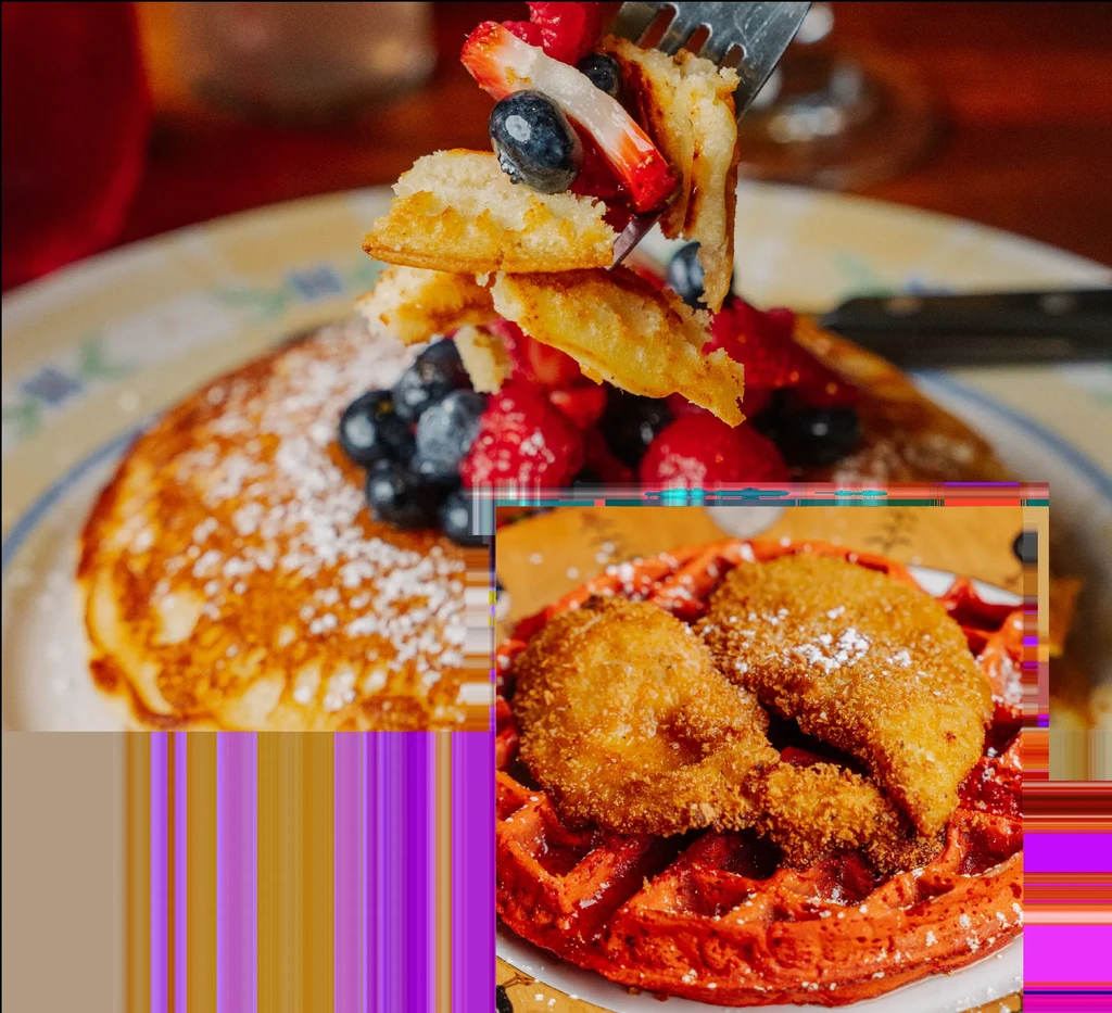 A fork lifts waffle pieces with berries over pancakes and chicken on a red waffle.