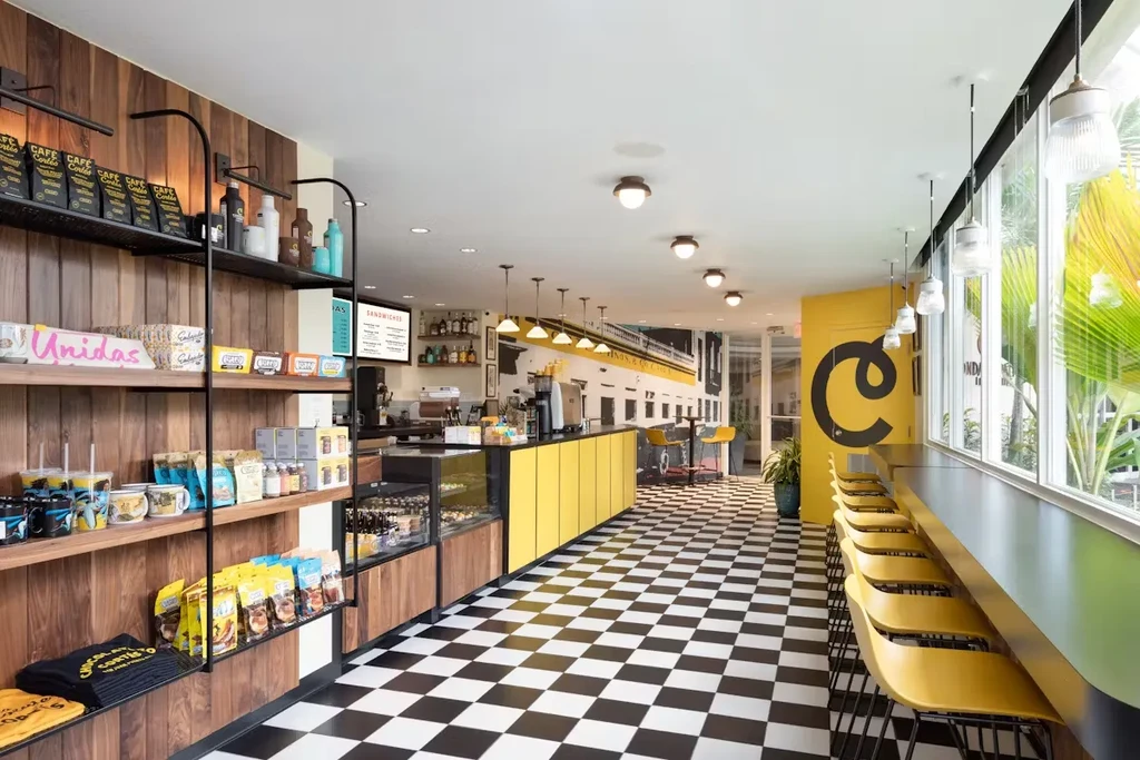 Cafe interior with checkered floor, yellow counter, and merchandise shelves.