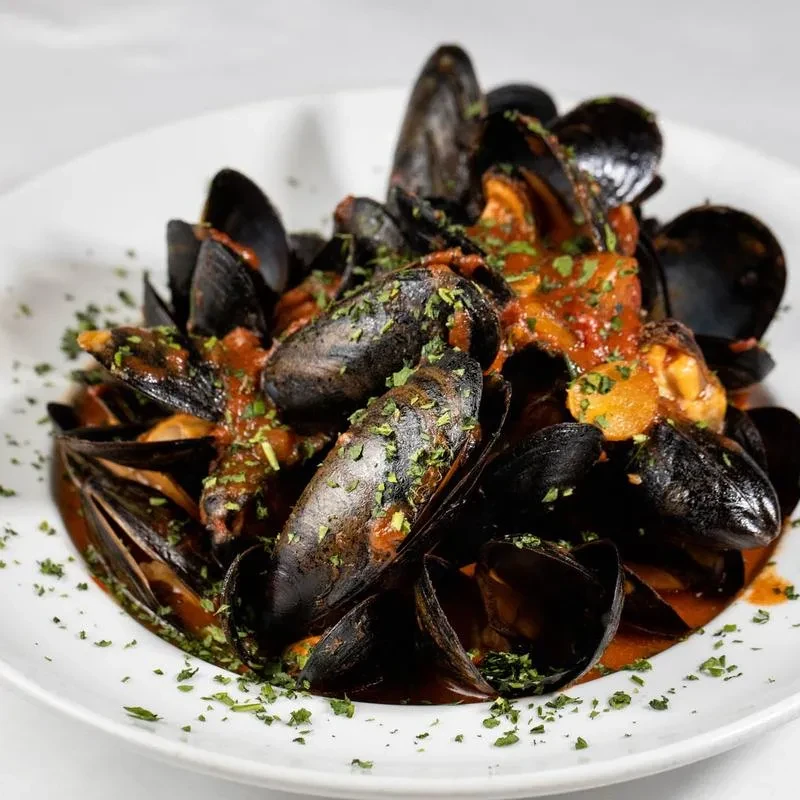 A white bowl filled with steamed mussels in red sauce.