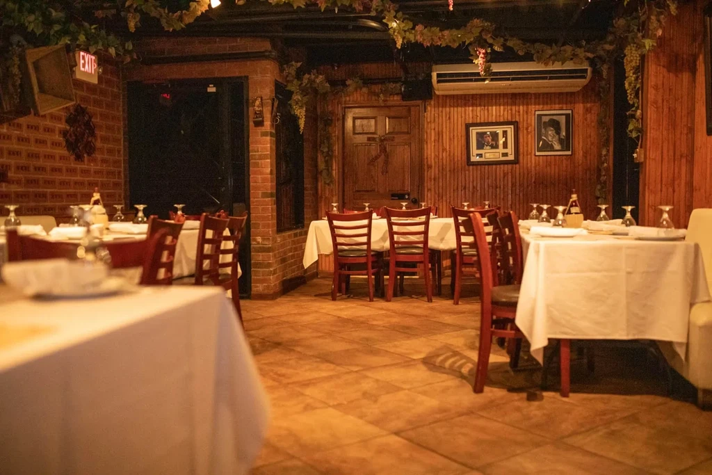 A restaurant dining room with white tablecloths, wooden chairs, brick, and wood walls.