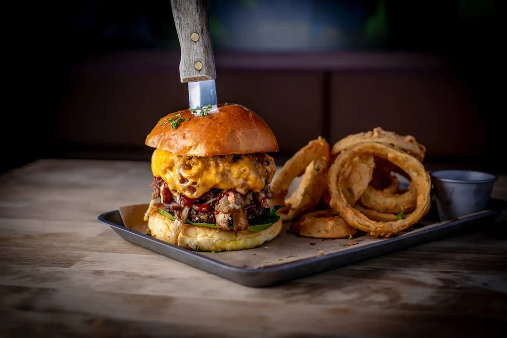 A cheesy burger with a knife, and a side of onion rings.
