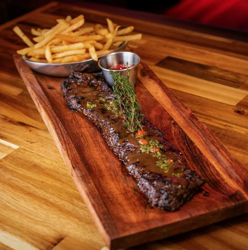 Grilled steak with sauce, fries, and thyme on a wooden platter.