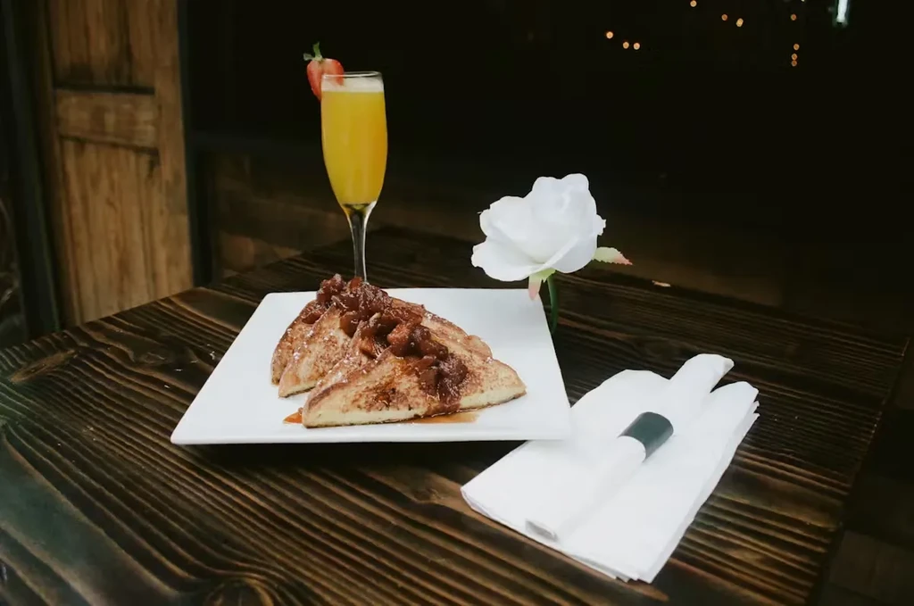 French toast, mimosa, and a white rose on a wooden table.