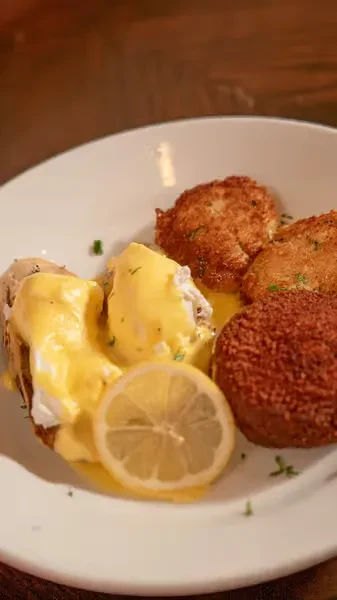 Crab cakes and eggs Benedict with hollandaise sauce and a lemon slice.