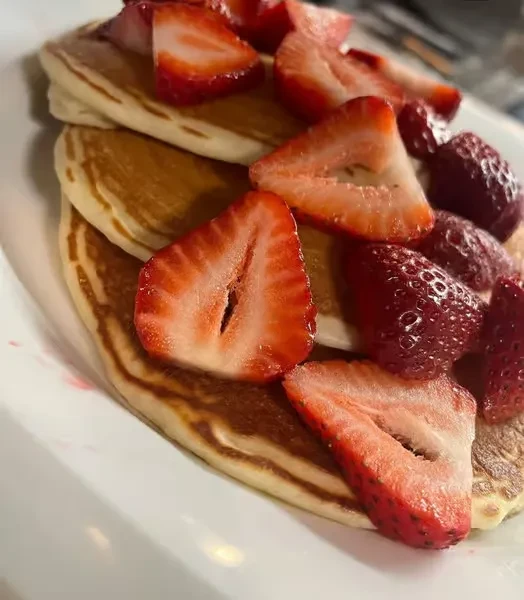 Close-up of fluffy pancakes topped with whole and sliced strawberries.