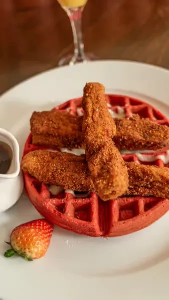 Red velvet waffle with fried chicken tenders, syrup, and a strawberry.