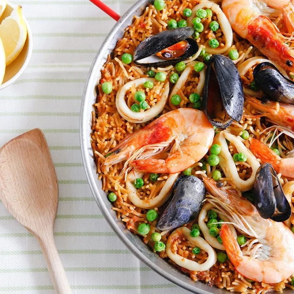A pan of paella with shrimp, mussels, squid, and green peas.