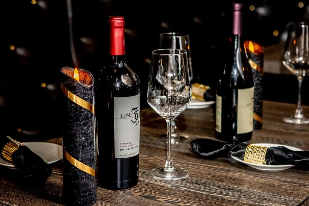 Two bottles of red wine, glasses, and a candle on a wooden table.