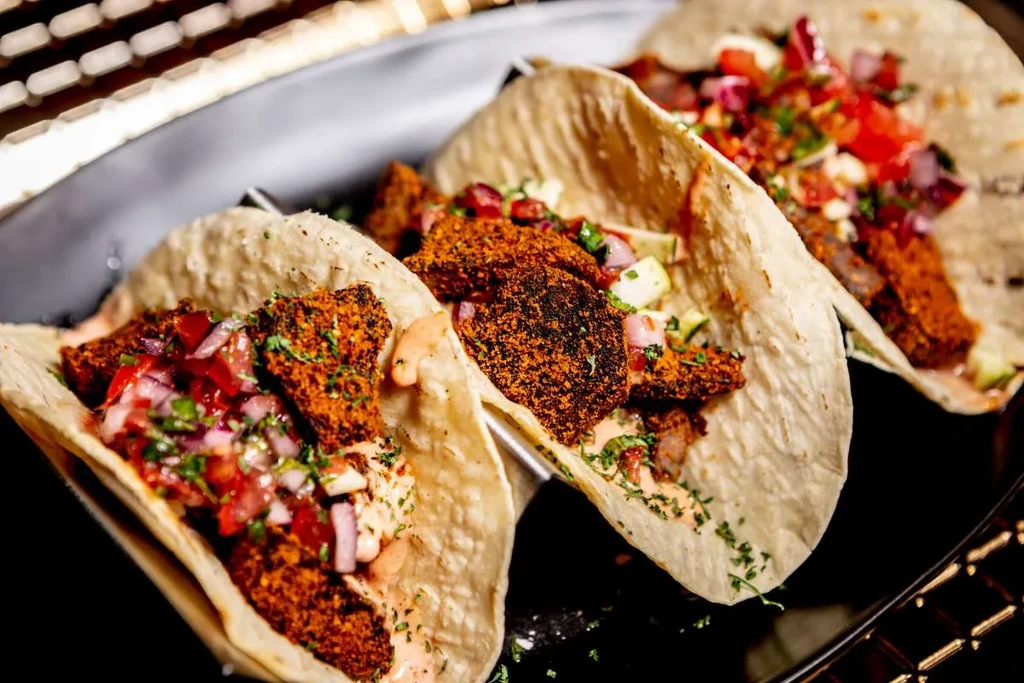 Three tacos with spiced meat, salsa, and sauce on a black plate.