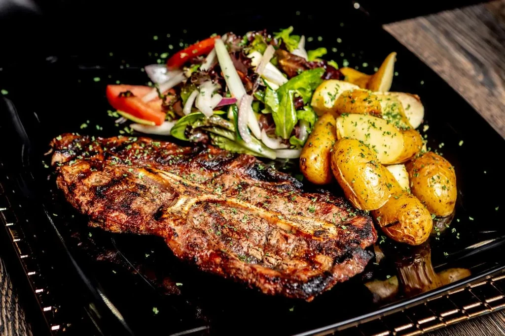 Grilled T-bone steak with roasted potatoes and a side salad.