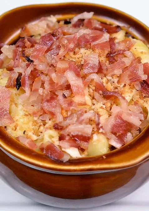 A brown bowl filled with mac and cheese topped with bacon.