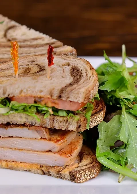 A large turkey club sandwich with greens and sliced tomatoes.