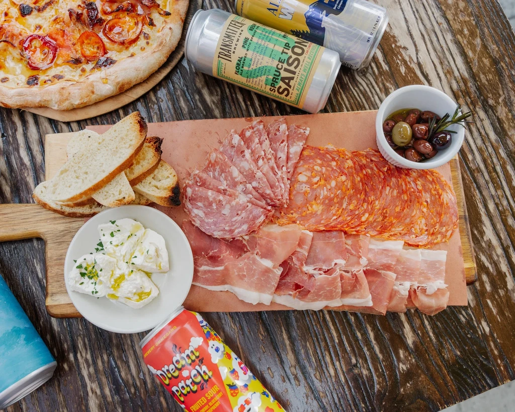 Pizza, charcuterie board, bread, and cheese with various craft beer cans.