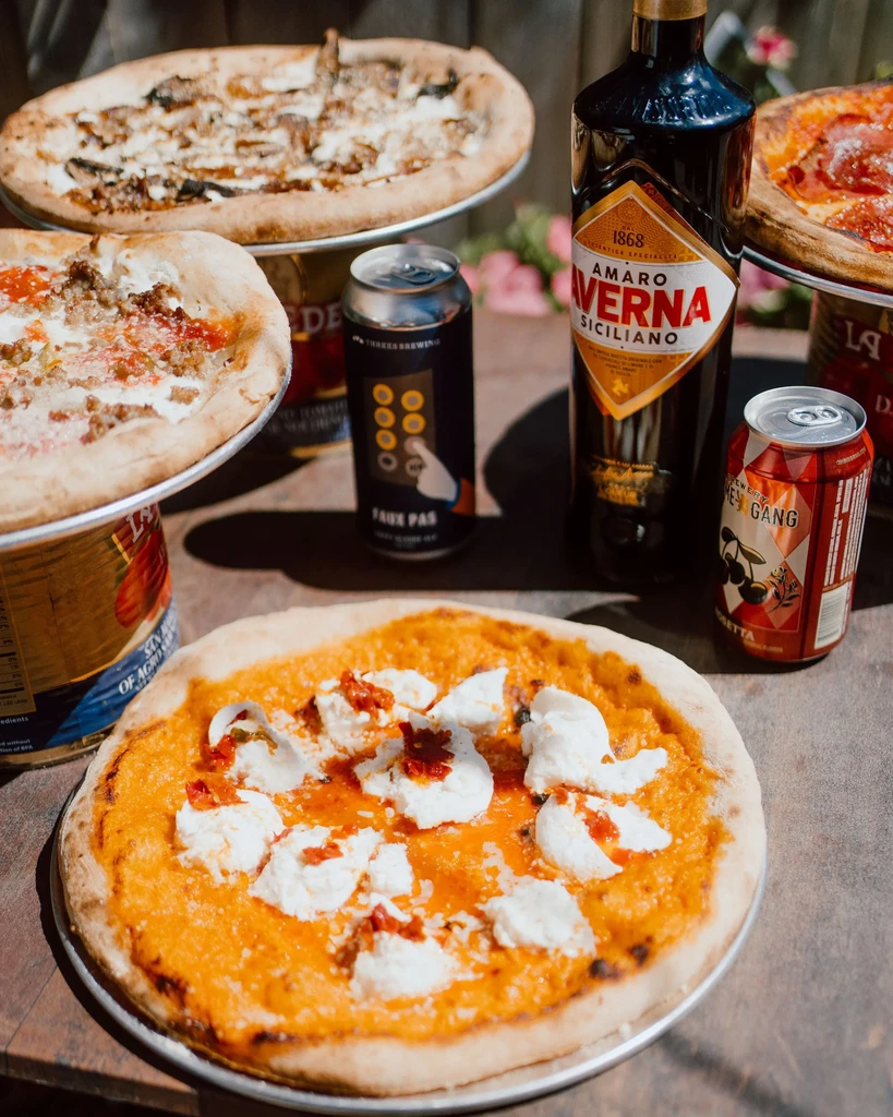 Three pizzas, two beer cans, and a bottle of Amaro Verba Siciliano.