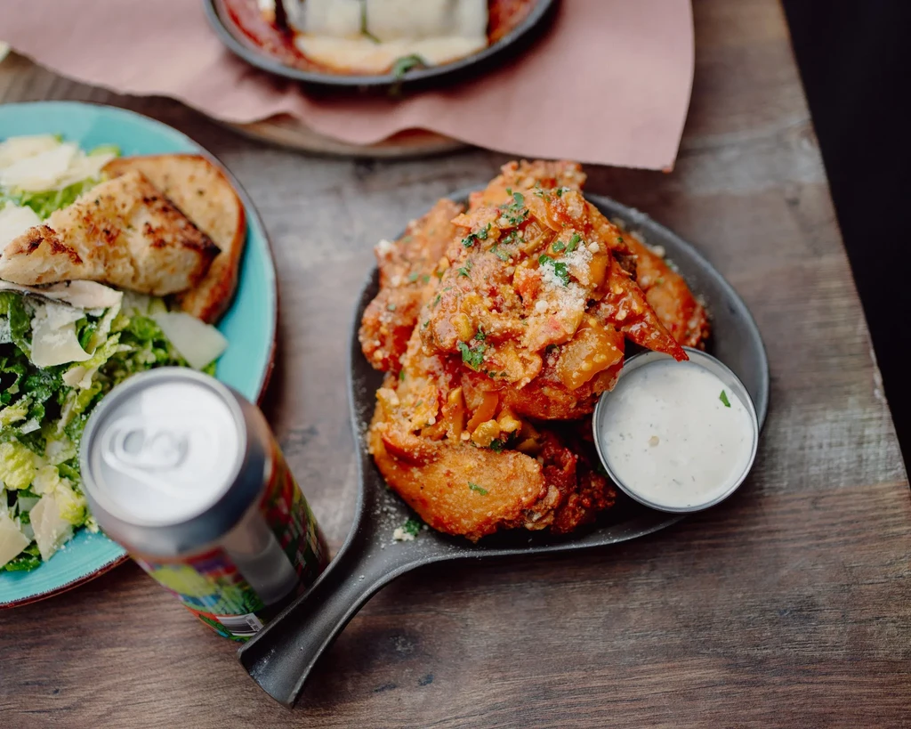 A cast-iron skillet of chicken wings, salad, and a soda can.