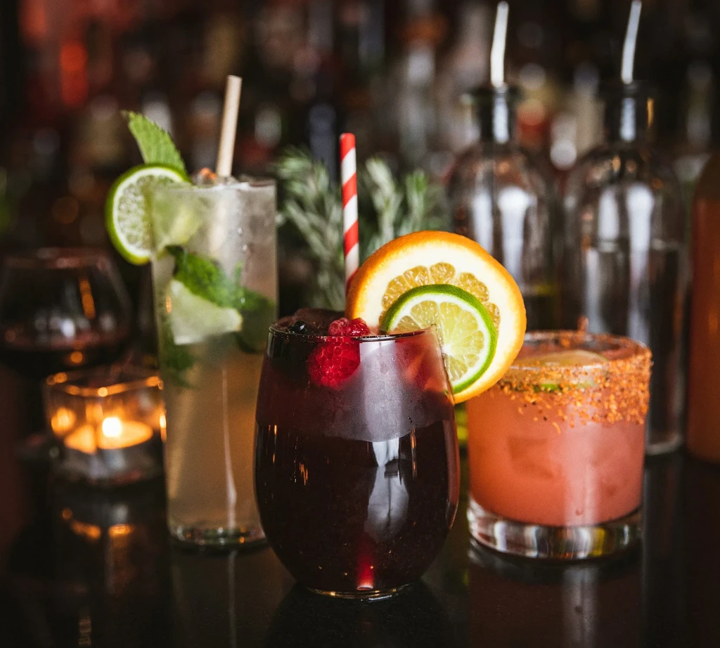 Three cocktails on a bar counter with bottles and a candle.