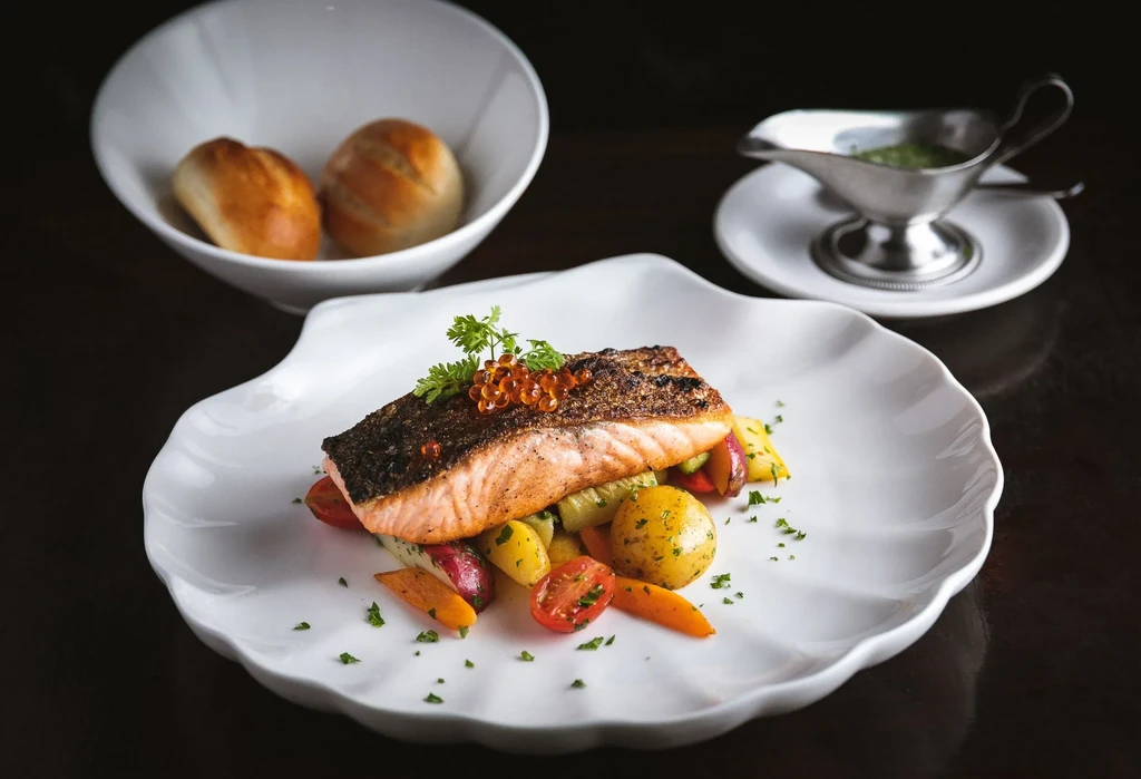 Pan-seared salmon with vegetables, garnished with caviar and parsley, with rolls.