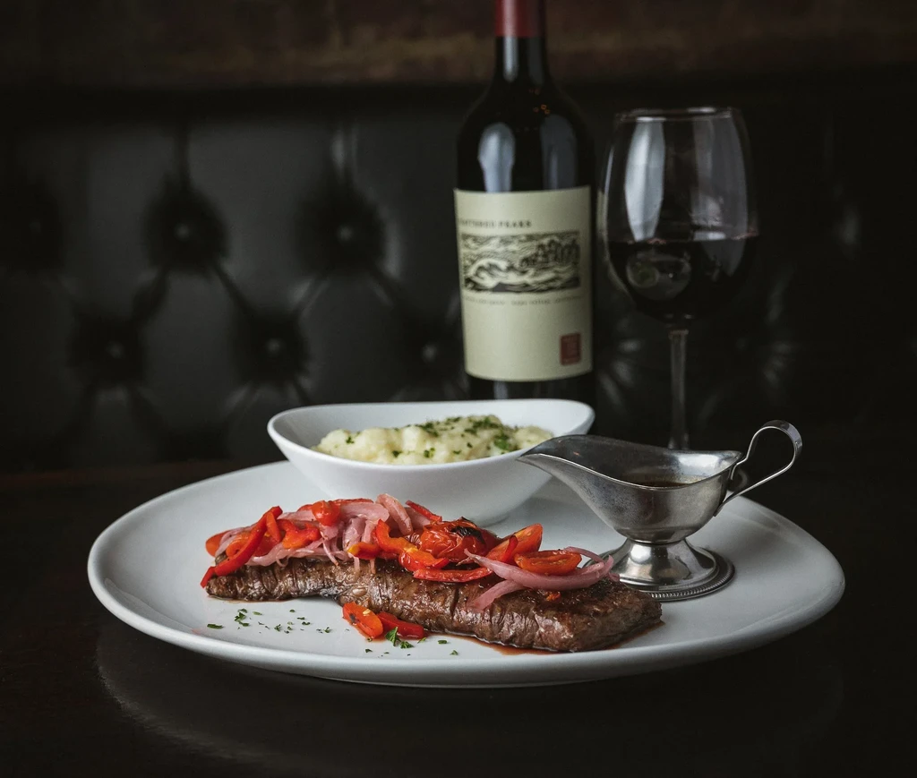 Steak with roasted peppers and onions, mashed potatoes, and red wine.