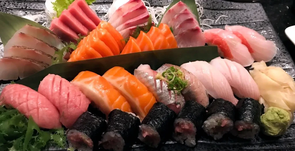 A platter of various sashimi, sushi, and maki on a dark plate.