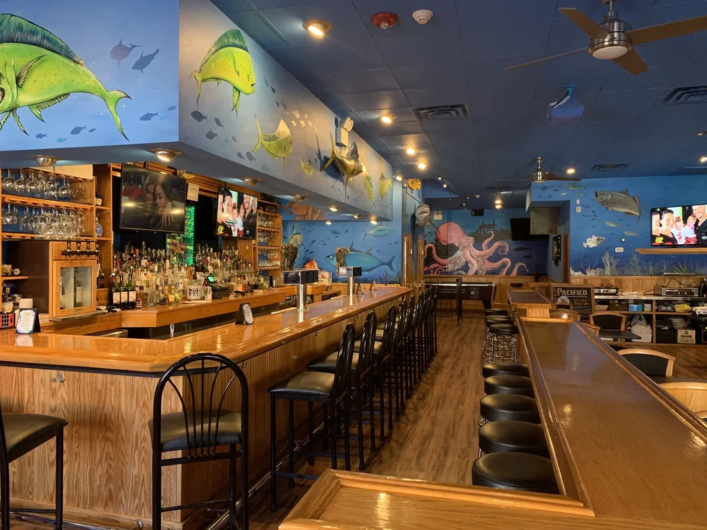 A vibrant bar with ocean-themed murals, a long bar, and pool table.