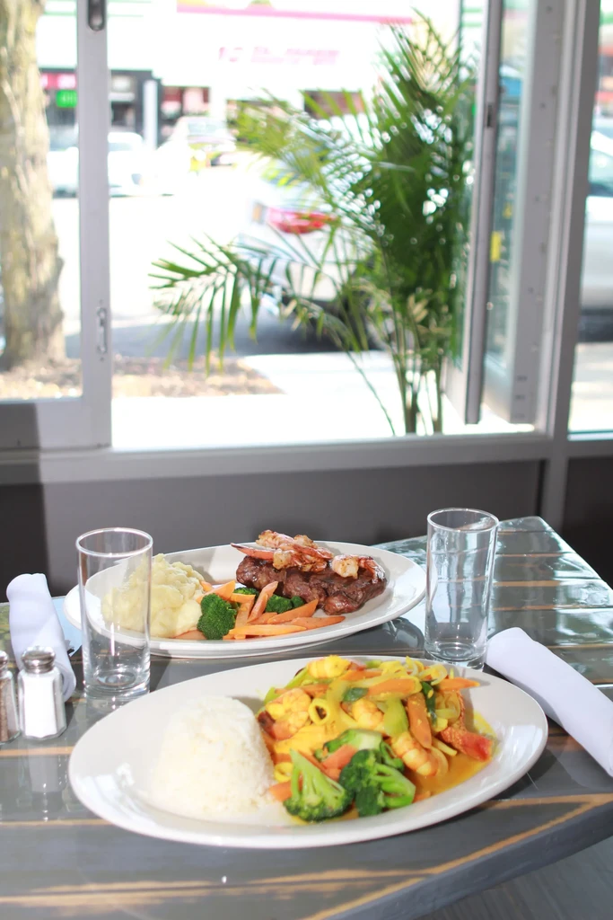 Two restaurant meals are on a table by a large window.