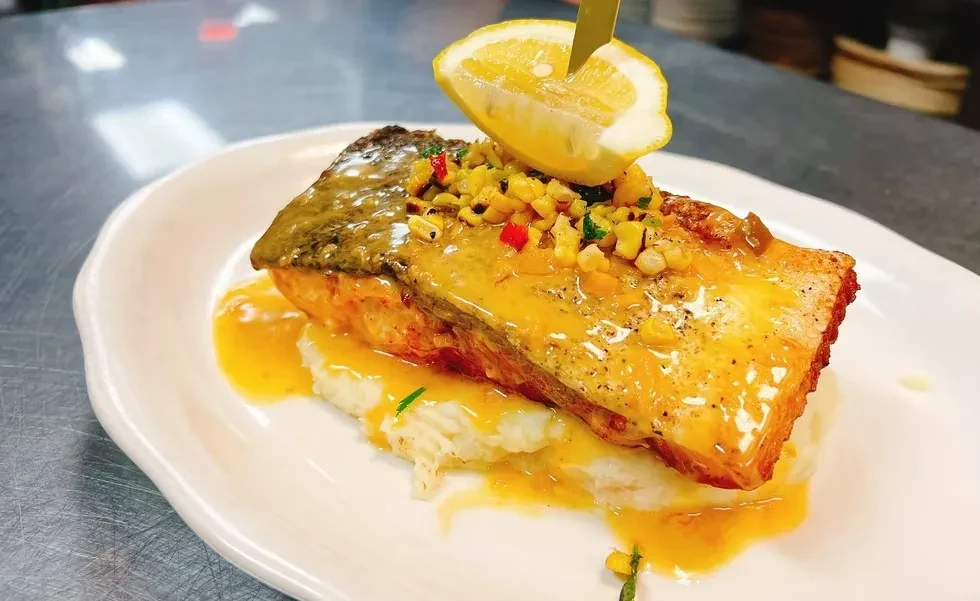 Salmon fillet with corn salsa, lemon, and sauce on mashed potatoes.