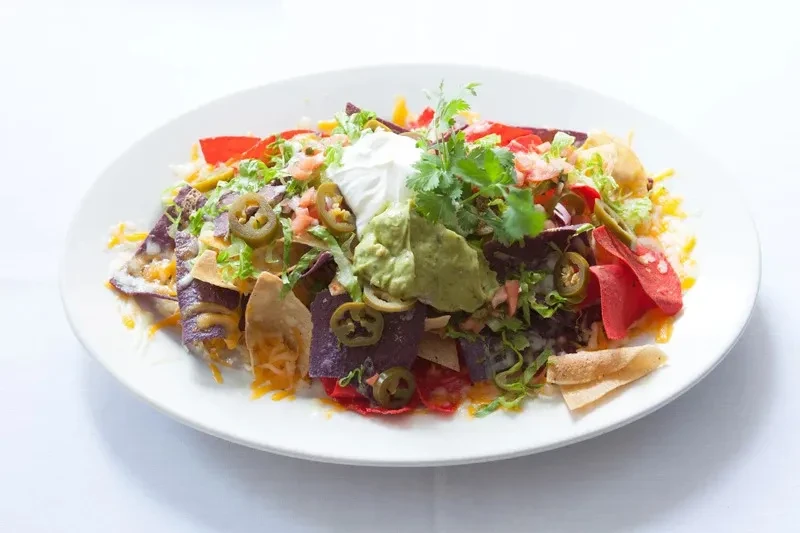 A white plate piled high with colorful nachos, topped with guacamole.