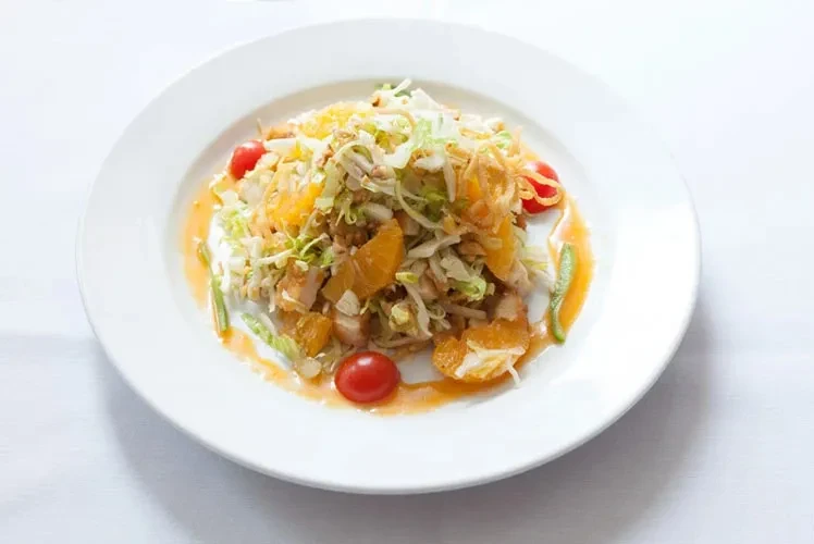 White plate with shredded chicken, lettuce, orange segments, and cherry tomatoes.