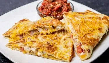 Three triangular chicken quesadillas with melted cheese and red salsa.